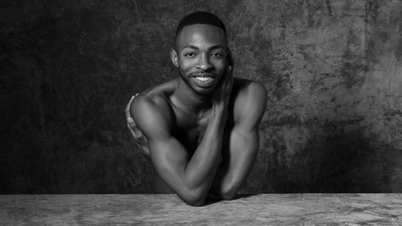 Josh Francique’s headshot (in black and white); Josh wraps his arms across his chest as he smiles
