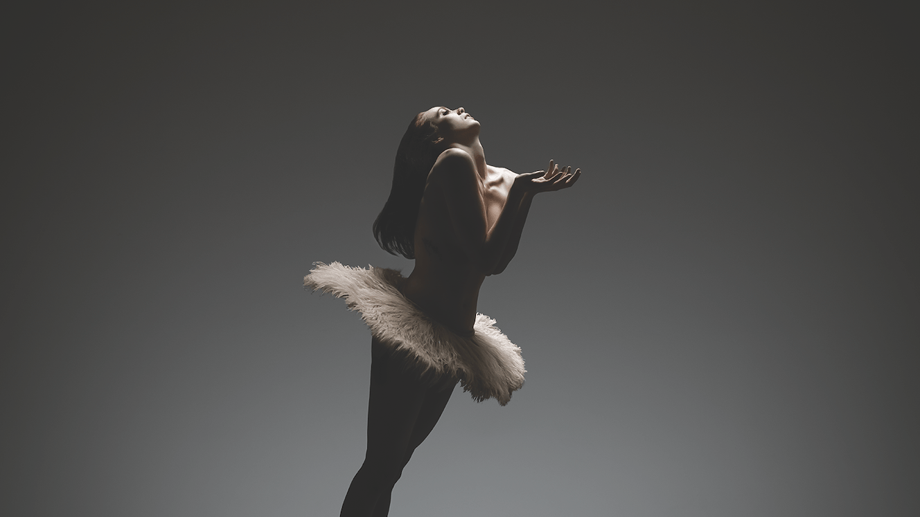 Alonzo King LINES Ballet Company Dancer Madeline DeVries on relevé, offering her hands forward while wearing a feathery tutu